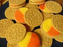 Das Bild zeigt aufgedrehte Oreo-Kekse mit Candy-Corn-Geschmack. Die oberen Hälften sind goldfarben und haben das typische Muster der Marke (mehrere Kreise, die von jeweils vier Dreiecken umgeben sind). Der Oreo-Schriftzug ist mittig in einem Oval platziert. Auf den unteren Kekshälften befinden sich je ein gelber und ein oranger Halbkreis.