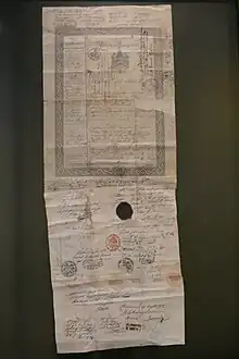 Fotografie eines aus zwei Stücken Papier zusammengesetztes Dokument mit gedruckten und handschriftlichen Zeilen in unterschiedlichen Schreibrichtungen, mehreren Stempeln und Siegeln