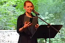 Cia Rinne an einem Lesepult stehend, ein geöffnetes Buch in der Hand