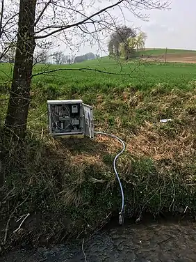 Das Foto zeigt einen automatischen Probenehmer, der an der Böschungskante eines Kleingewässers installiert ist