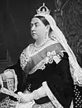 Queen Viktoria mit Krone, Spitzenschleier, Juwelenhalsband, schwarzem Taftjäckchen mit Trompetenärmeln, Ordensband, Orden, Fächer; Fotografie, um 1880