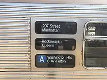 Gesickte Stahlseitenwand eines U-Bahn-Zugs, drei Rollbandfelder mit weißer Beschriftung auf schwarzem Grund: „207 Street Manhattan / Rockaway Queens / (A) Washington Hts 8 Av-Fulton“
