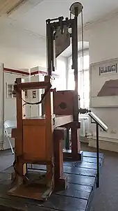 Guillotine, Baujahr 1946 und im Ausstellungsraum des Museums stehend, besteht aus einer Holzbank mit vorgelagertem Schlitten, auf dem der Verurteilte fixiert, in die Horizontale gebracht und mithilfe von auf der Unterseite befestigten Rollen auf der Holzbank nach vorne bis zum Kopfteil gezogen wird. Kopfteil besteht aus einer hölzernen Halskrause, die angehoben werden kann, einem Auffangbehältnis für den Kopf und einem circa drei Meter hohem Eisengerüst, an dem das, an einem Gewicht befestigte Fallbeil hängt, dass durch einen Hebel an der Seite des Kopfteils gelöst wird, als Objekt im Strafvollzugsmuseum ausgestellt