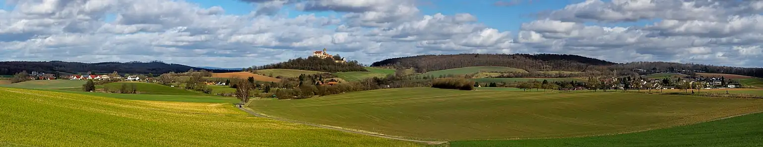 Landschaftsbild bei Altwiedermus (links) und Neuwiedermuß (rechts) mit der Burg Ronneburg links der Bildmitte. Rechts der Burg der Steinkopf im Ronneburger Wald. Hinter Altwiedermus Teile des Marköbeler Bergrückens.