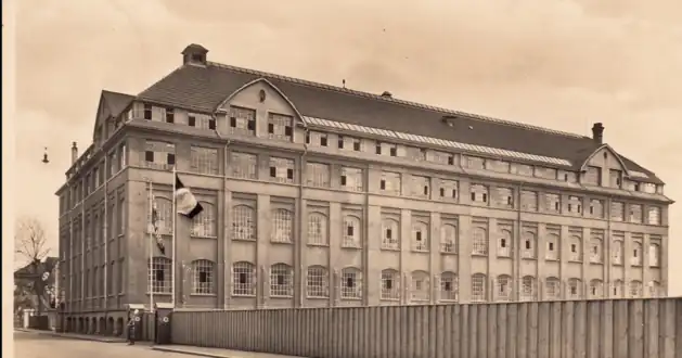Ansicht Schrammstraße.Die Cramerstraße verläuft längs des Zauns. Die Fabrikanlage wurde kurz nach der Insolvenz von 1932 vom Reichsarbeitsdienst genutzt, mit Absperrung des westlichen Abschnitts der Schrammstraße, mit Torwache mit Spaten (siehe Bildvergrößerung)