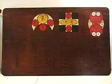 Dunkelbraune Holztafel mit drei farbigen Geometrie-Illustrationen (einander berührende und durchdringende Kreise und Quadrate) und schwarzen japanischen Schriftzeichen
