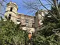 Verwachsene Eingangsfront mit vorgelagertem Treppenhaus und oktogonalem Eckturm.