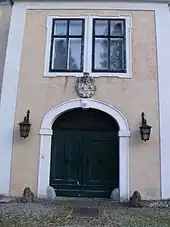 Frontalansicht des Torbaus mit einem korbbogigen Tor, darüber ein steinernes Wappenrelief und ein gekuppeltes Fenster
