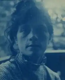 Helle und dunkle Blautöne zeigen eine Porträtaufnahme von Susan Macdowell Eakins. Sie hat langes dunkles Haar, das locker zusammengebunen ist.