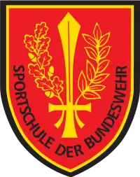 Das heutige Verbandsabzeichen der Sportschule der Bundeswehr, im aktuellen Design. Öl- und Eichenzweig umhüllen wie ein Kranz ein aufrechtstehendes Schwert