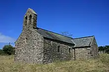 Eine einfache steinerne Kirche mit Schieferdach mit einem Glockenstuhl auf dem Giebel. Das Querschiff ist rechts im Bild.