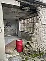 Zerstörter Eingang mit der Tür auf dem Boden. Das Ölfass war nicht Teil der Ausstattung.