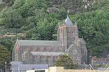 Eine große Kirche mit Obergaden steht vor einem Hügel, links davon befindet sich ein Kirchturm mit Pyramidendach.