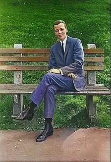 Stormé DeLarverie sitzt mit übergeschlagenen Beinen auf einer braunen Parkbank. Sie trägt ein Jackett und eine Hose aus jeansblauem Tweed, ein weißes Hemd, eine schwarze Krawatte und schwarze Stiefeletten. Ihre Hände ruhen ebenfalls übereinandergeschlagen auf ihrem Schoß, zudem hält sie in der linken eine Zigarette. Ihre braunen Haare trägt sie als bis zu den Ohren geschnittene Stoppelfrisur. Im Hintergrund ist eine grüne Wiese zu sehen, im Vordergrund ein hellbrauner Gehweg.