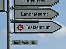 Das Foto zeigt ein richtungsweisendes Verkehrszeichen mit COVID-19-Symbol und Text „Testzentrum“