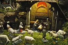Aus Holz geschnitzte Figuren. Im Vordergrund mehrere Schafe, dahinter die Heilige Familie mit dem Jesuskind in der Krippe.