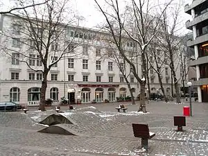 Pflasterwellen mit Wasserspiel, Platanen, Stühle am Nordende. Rechts die Hamburgische Landesbank (heute Hamburg Commercial Bank). Hinten über die gesamte Breite das Thalia Theater.