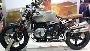 Frontale Farbfotografie von einem grauen Motorrad mit braunem Sitz und dem BMW Logo auf dem Tank.