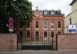 Thebäerstraße 51: ehemaliges Schulhaus des Vororts St. Paulin; siebenachsiger sogenannter Rohbau: Stichbogenfenster und Brüstungsfelder hell abgesetzt vom kleinteiligen Sandsteinquadermauerwerk, 1872, Architekt A. Massing, 1884 verlängert