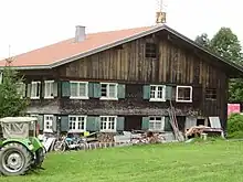 zweigeschossiger, verschindelter Blockbau mit flachem Satteldach, zum Teil Schubflügelfenstern und Klebdächern