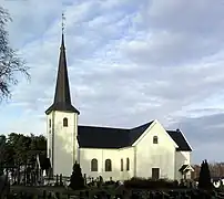 Foto einer weißen Holzkirche, im Vordergrund ein Friedhof