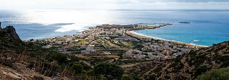 Halbinsel von Paleochora an einem Sonnigen Tag. Es sind viele Gebäude und Straßen sichtbar, welche links und rechts von einem Strand eingeschlossen sind.