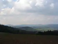 Südwestliche Weschnitzpluton-Region von der Tromm (Auf der Lehen) aus. Hintergrund: Wachenberg (links) bis Kreuz-Berg (rechts). Vordergrund: mit G2-Scherben übersäter Acker (Durchtrümmerung des Trommgranits), dahinter Hügel der Trommgranit-Gneis-Mischzone zwischen Mörlenbach und Stallenkandel