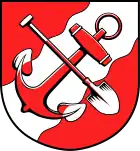 In Rot ein schräglinker silberner Wellenbalken, den, schräglinks gekreuzt, ein Anker mit Ring und ein Spaten in verwechselten Farben überdecken (Brunsbüttel, DE)