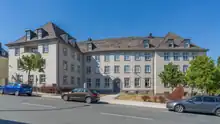 Das Foto zeigt das Gebäude des Wasserwirtschaftsamt in Hof (Saale). Es ist schlicht, hat links einen Vorbau und 3 Fensterreihen über die Fassade hinweg