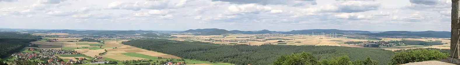 Nordostblick von der Weidelsburg: Links vorne der Ippinghäuser Grund mit Ippinghausen und dem tiefer gelegenen Weiler Leckringhausen, schräg rechts dahinter Wolfhagen und der Ofenberg (372,5&nbsp;m; 6,8&nbsp;km entfernt) rechts der Stadt und am Westrand des Altenhasunger Grabens; weiter rechts der Isthaberg (523,1&nbsp;m; 7,1&nbsp;km) und schließlich die Isthaebene mit Bründersen vor Istha vor Oelshausen (Mitte) und Altenstädt vor Balhorn (rechts), die zum Ippinghäuser Grund hin vom bewaldeten  Rauenstein gerahmt wird. Hintere Reihe: Links hinter den Windkraftanlagen Stromberg (362,2&nbsp;m; 14,0&nbsp;km) und Heidelbeerenberg (398&nbsp;m; 13,3&nbsp;km), rechts dahinter der Desenberg (343,6&nbsp;m; 25,6&nbsp;km); links des Ofenbergs der Warteberg (419&nbsp;m; 9,8&nbsp;km), zwischen beiden der Escheberg (448,9&nbsp;m; 16,0&nbsp;km); in der Bildmitte, hinter dem Isthaberg, der Große Bärenberg (600,7&nbsp;m; 12,3&nbsp;km) mit Funk- und Aussichtsturm, weiter rechts der Dörnberg (578,7&nbsp;m; 16,7&nbsp;km); hinter den Windkraftanlagen schließlich der Hohe Habichtswald (614,8&nbsp;m; 15,1&nbsp;km) und rechts der Schwengeberg (556,7&nbsp;m; 14,0&nbsp;km).Für eine detailliertere Beschreibung siehe Weidelsberg#Aussicht!