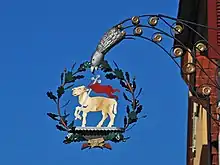 Ein am Gebäude befestigter Wirtshausausleger mit einem goldenen Lamm umrahmt von einem Eichenblätterkranz