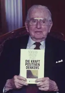 Norman Vincent Peale hält in seinen beiden Händen das Buch Die Kraft positiven Denkens, 1986 fotografiert