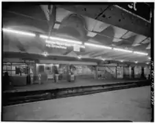 U-Bahnhof 96th Street um 1970 in einem Übergangsstadium mit Glühlampen und Leuchtstofflampen, mit noch weißem Unimark-Linienemblem auf schwarzem Stationsschild, mit noch nicht abgesperrtem oder vermauertem Seitenbahnsteig